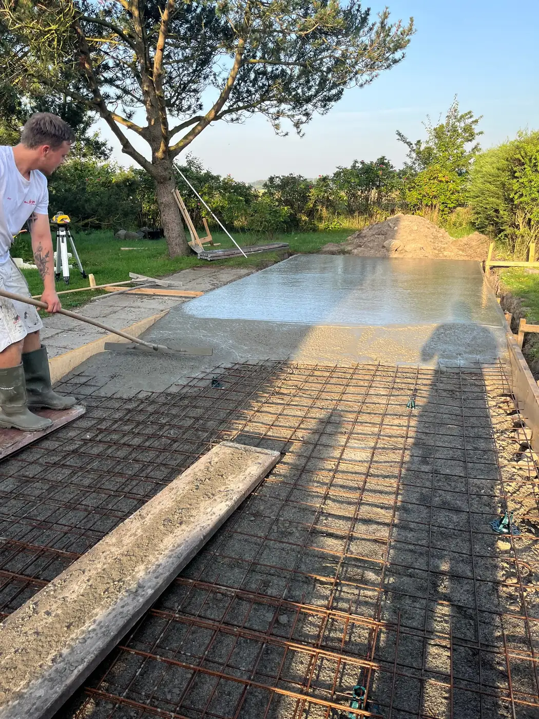 Betonarbejder traekker frisk beton ud over armeret stoebeplade udendoers