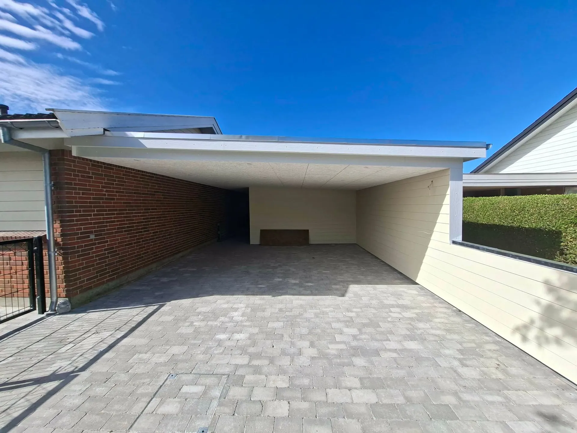 Ny carport set forfra med ny betonstensbelægning og rød murstensvæg