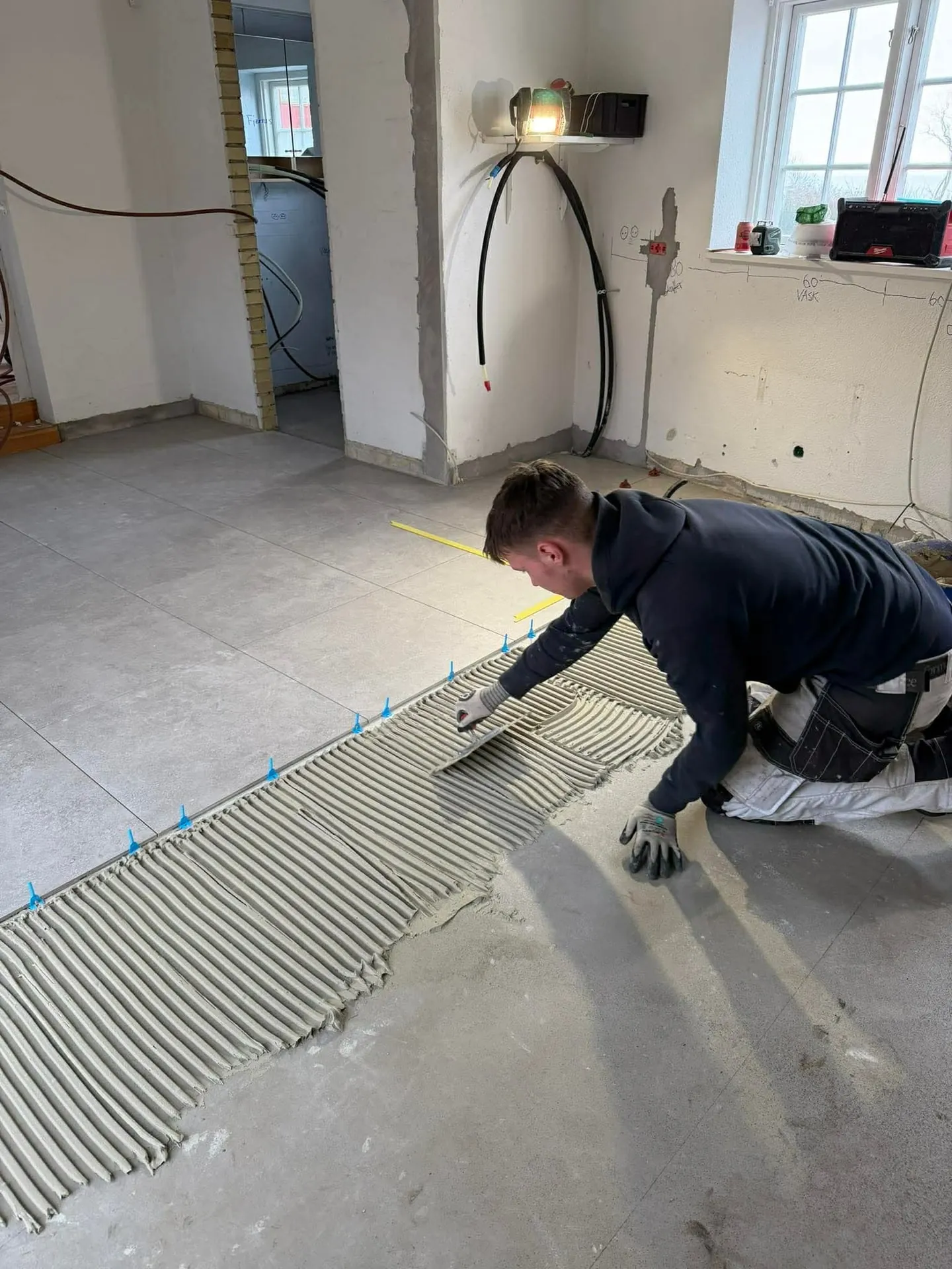 Haandvaerker traekker fliseklaeb ud med tandspartel foer store gulvfliser laegges