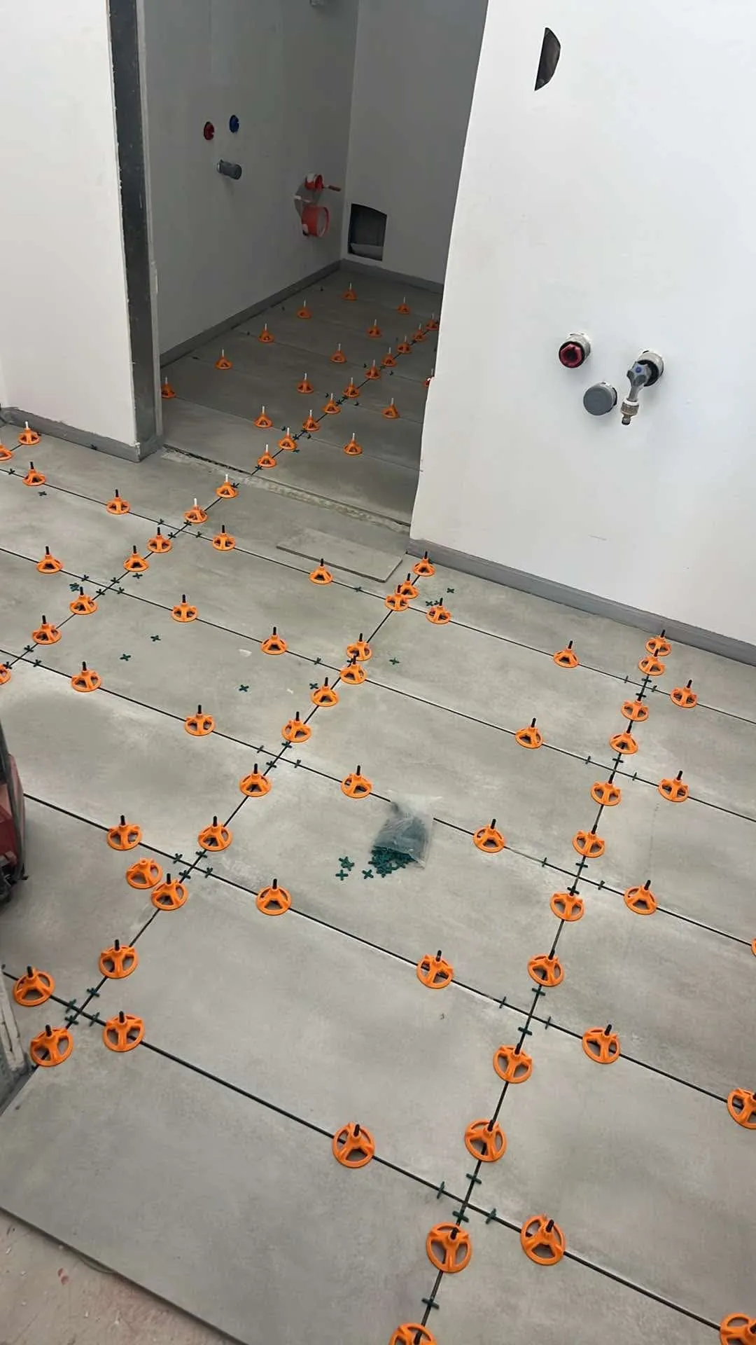 Nylagte grå gulvfliser med orange nivelleringsklips og fugekryds