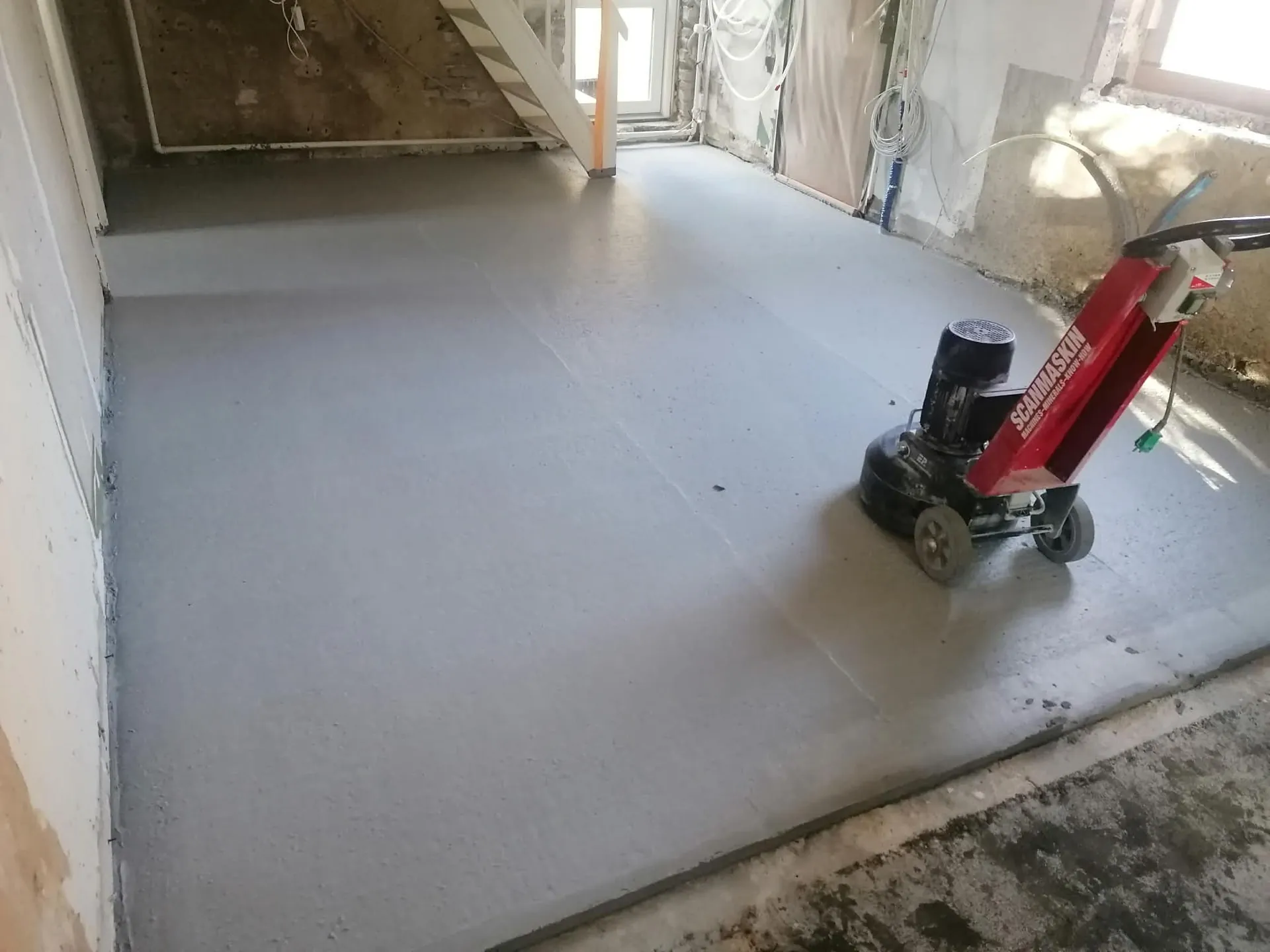 Nyafrettet gulv i et hus under renovering med slibemaskine stående klar