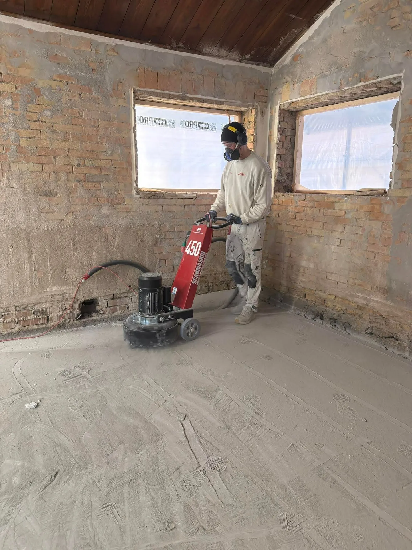 Medarbejder sliber betongulvet ned med gulvsliber i et rum under renovering