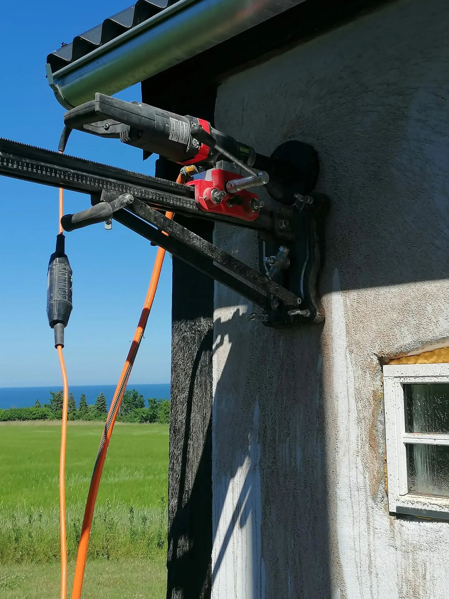 Borerig monteret på facade til kerneboring med udsigt over marker og hav