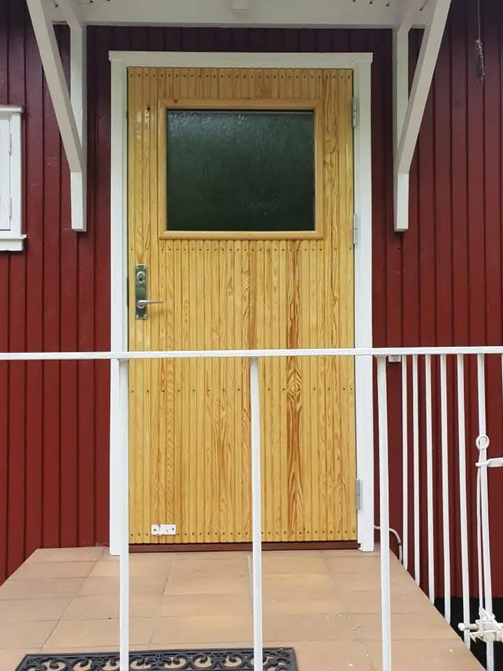 Snedkerbygget trædør med lille rude sat i rødt træhus med hvid karm