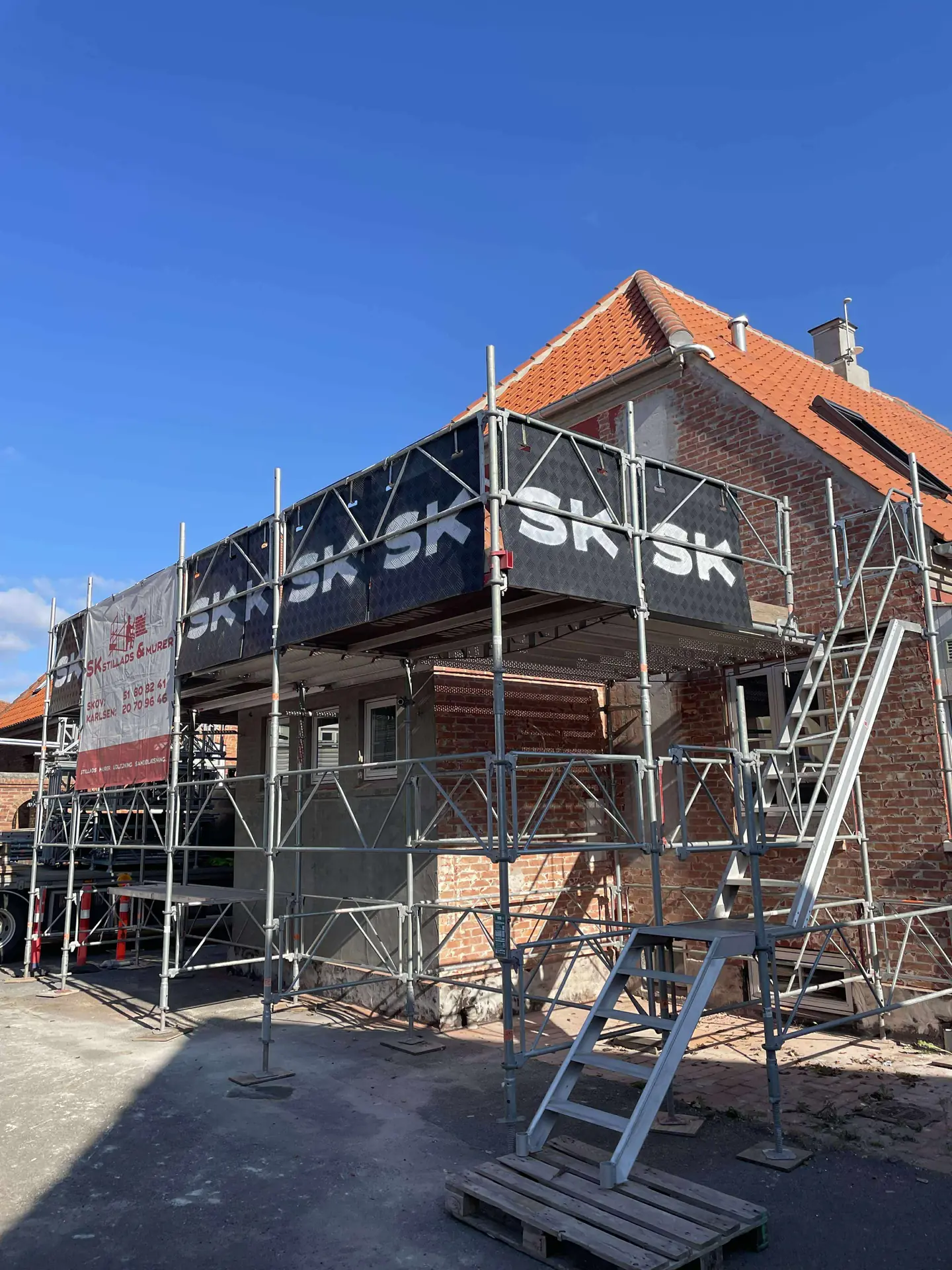 Rejst stillads langs murstensfacade under klar blå himmel