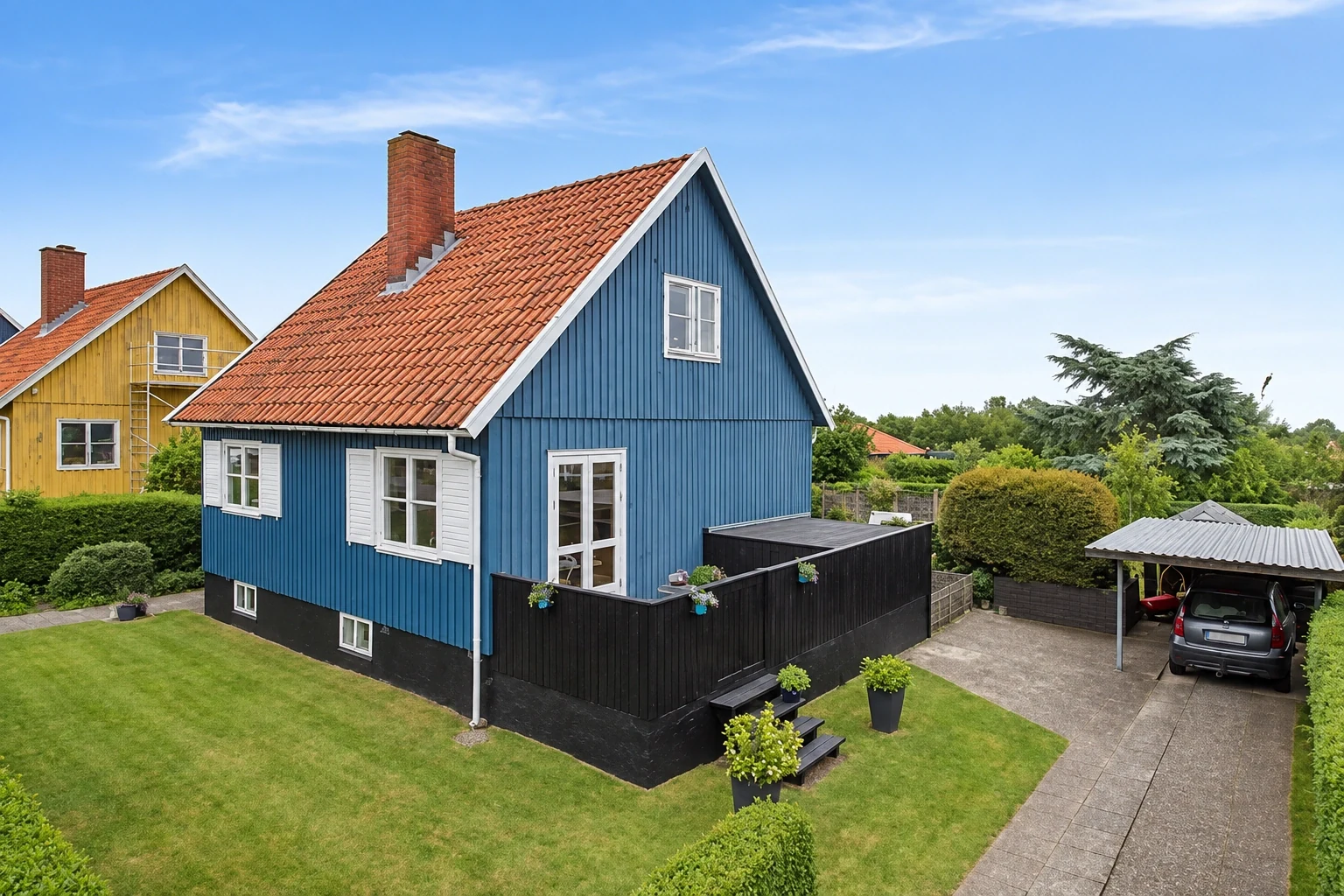 Blåt svenskerhus med hvide vinduer, sort sokkel og have