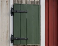 Grøn skodde med sorte smedebeslag ved vindue i rød facade