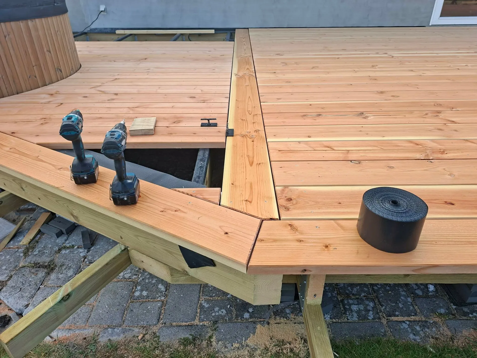 Nyt terrassedæk under opbygning med bjælkelag, kantbræt skåret i gering og hot tub bagved