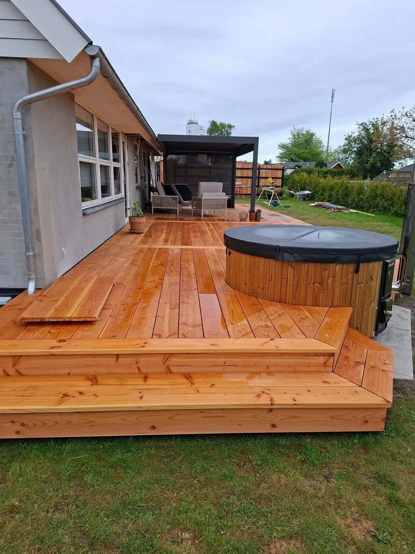 Færdig terrasse i lærk med brede trin ned mod græsplænen og hot tub
